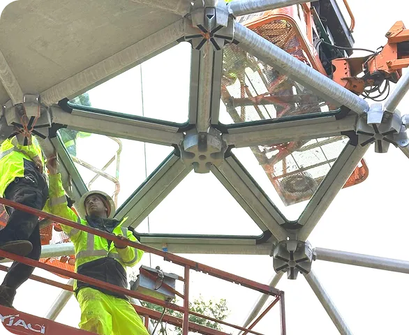 Construction team on scaffolding assembling geodesic dome structure with triangular glass panels