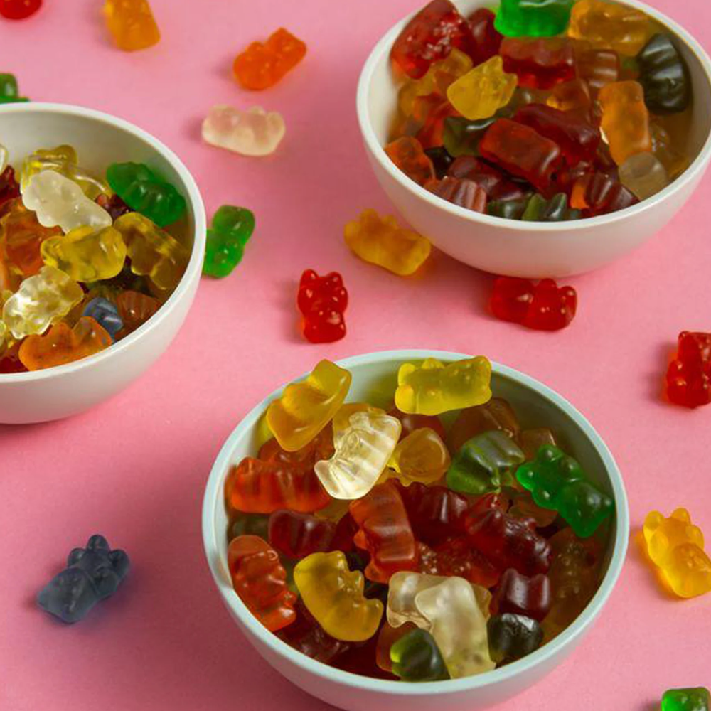 Three bowls of gummy bears on a pink surface.