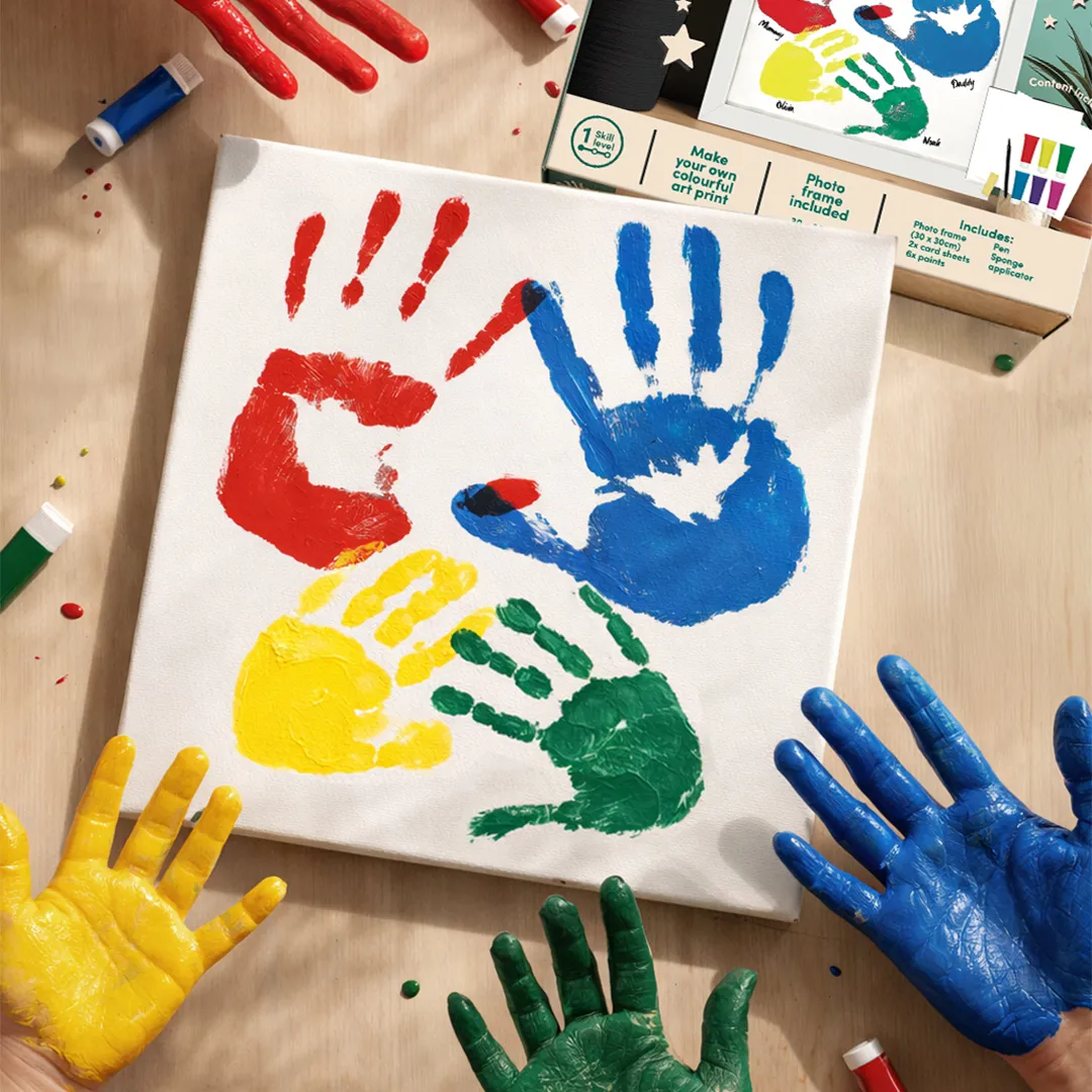 Four painted hands in red, blue, yellow, and green making handprints on a white canvas.