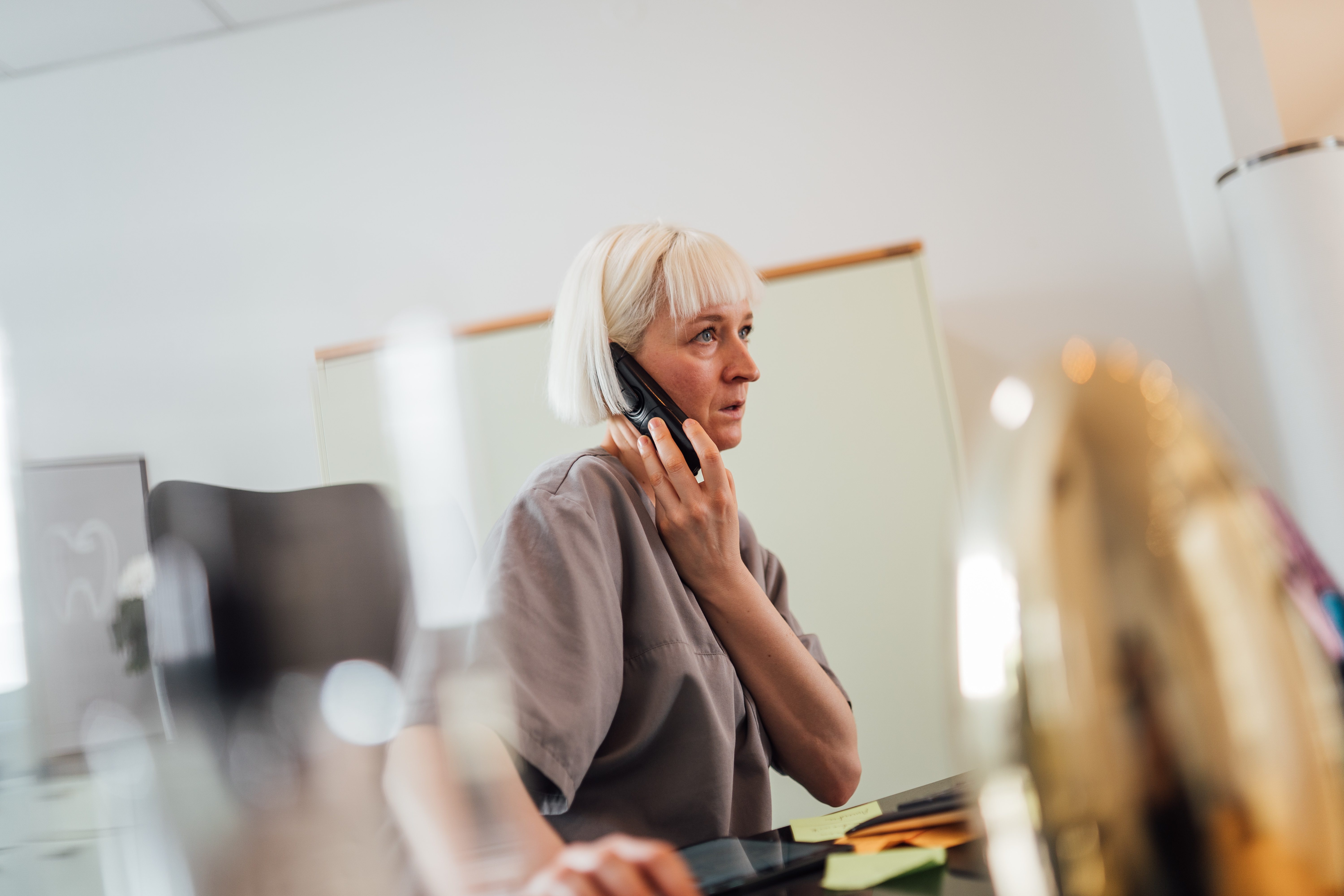 Woman with short blonde hair talking on a phone in an office setting.
