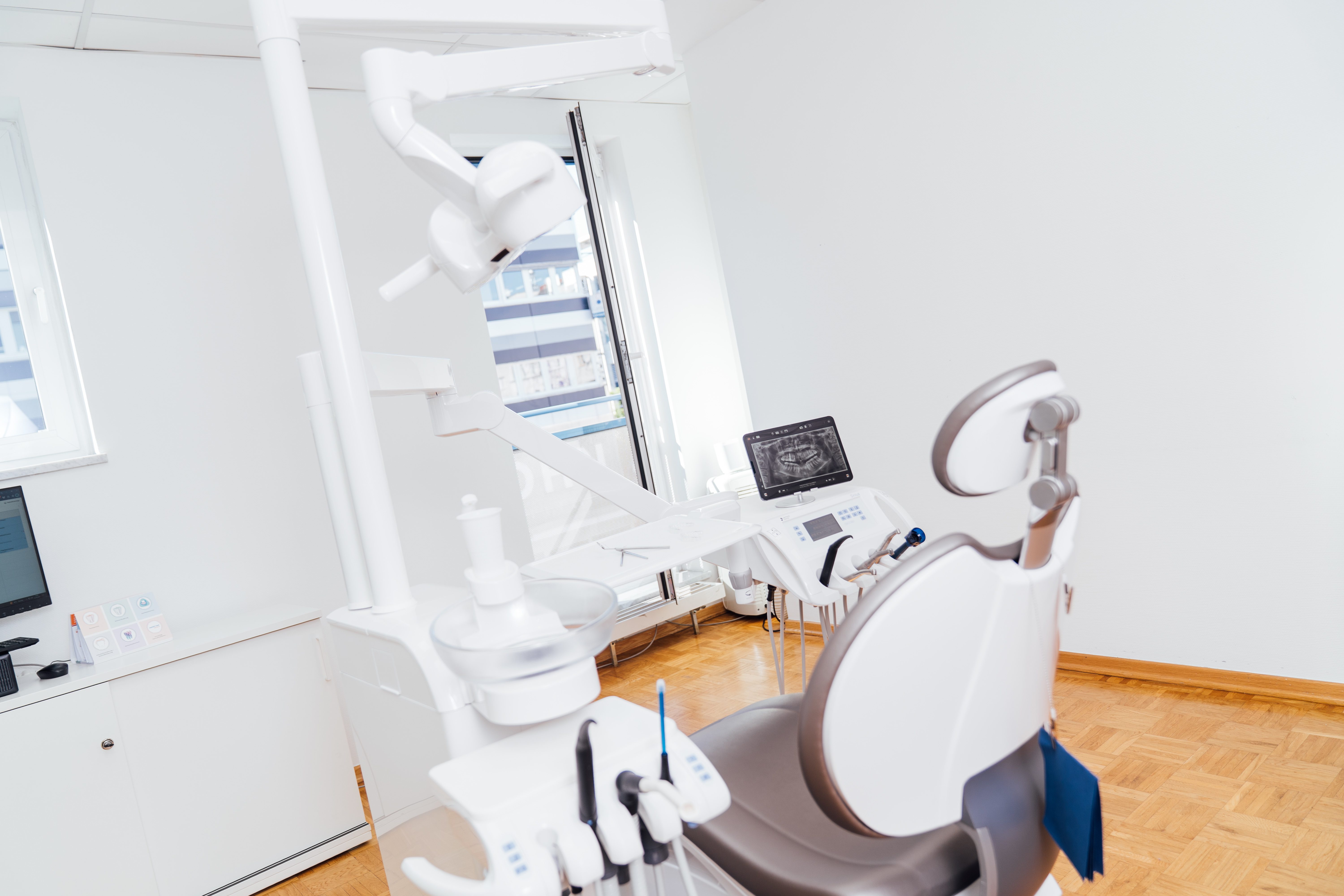 Modern dental chair with attached dental equipment and an X-ray image displayed on a monitor in a bright dental clinic.