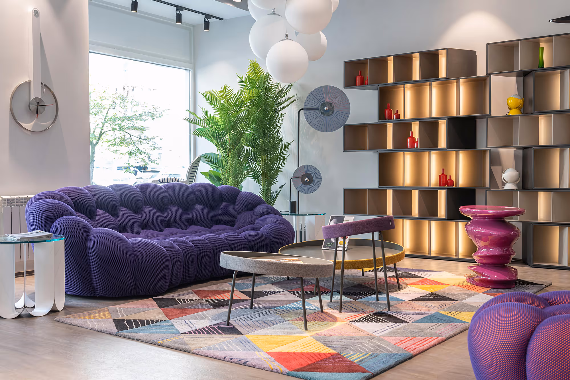 Modern living room with purple sofa, colorful rug, and open shelving