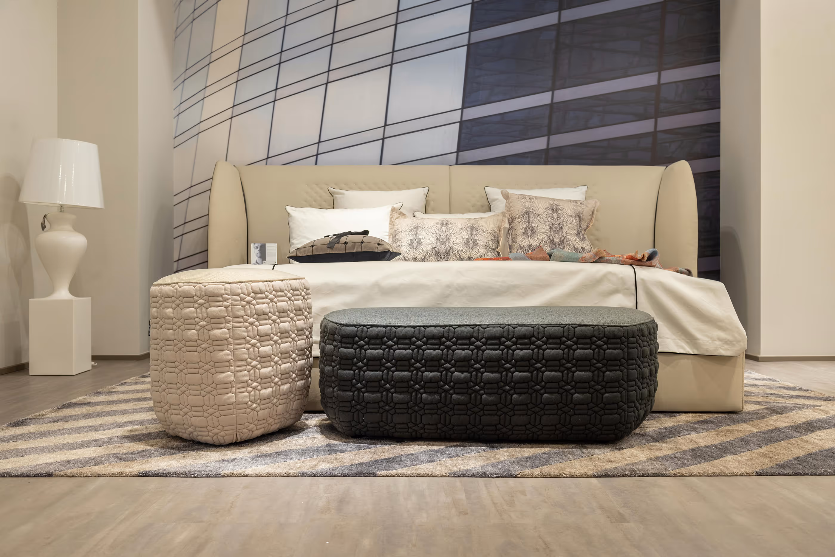 Beige upholstered bed with patterned pillows and ottomans