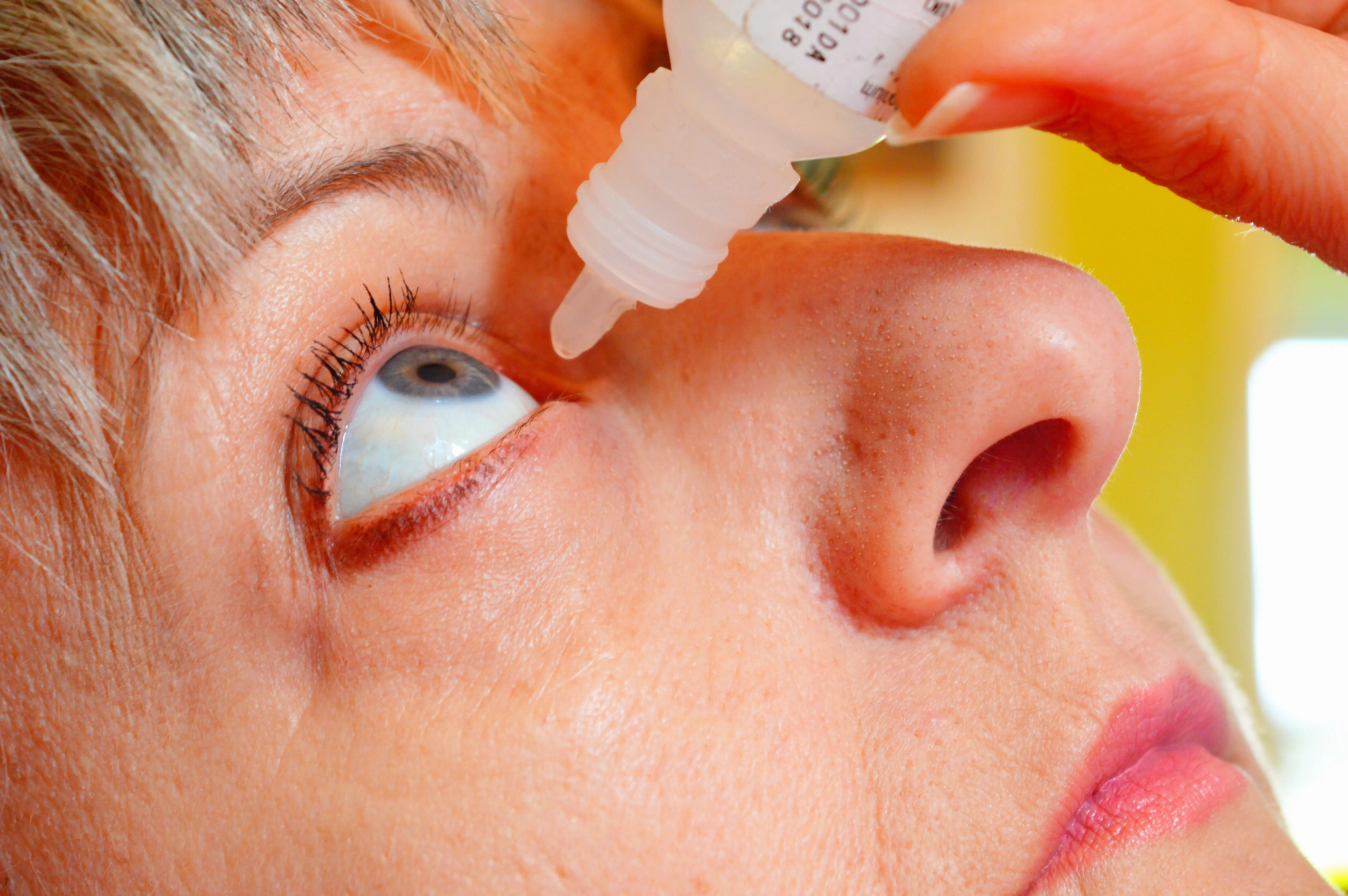 Person applying eye drops close-up with yellow background