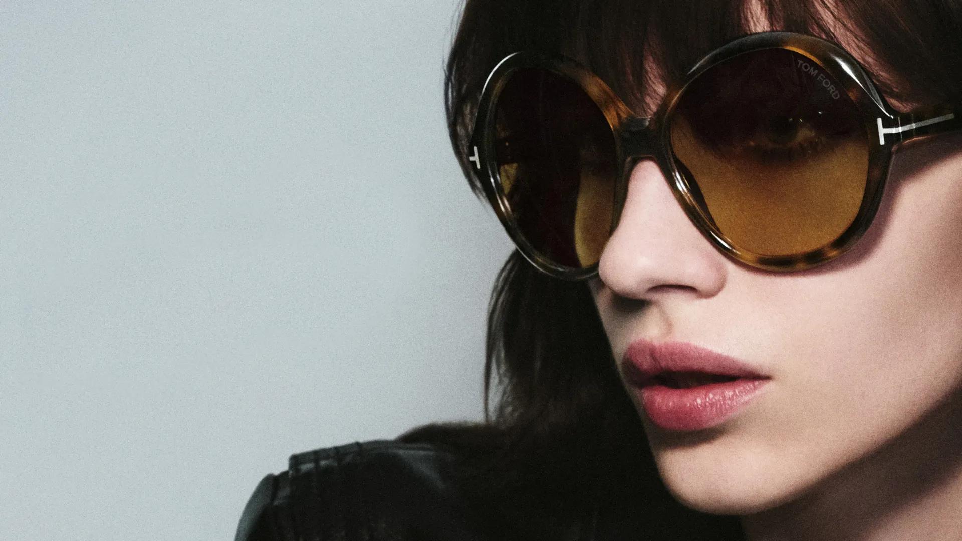 Woman in large tortoiseshell sunglasses looking stylish against gray background