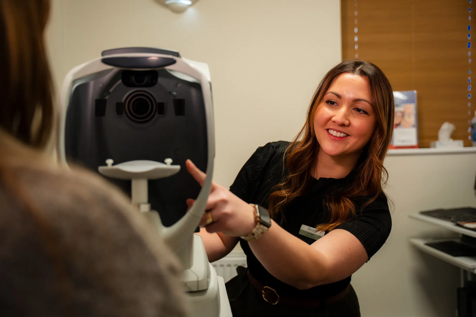Woman demonstrates 3D facial imaging camera equipment to patient in medical office