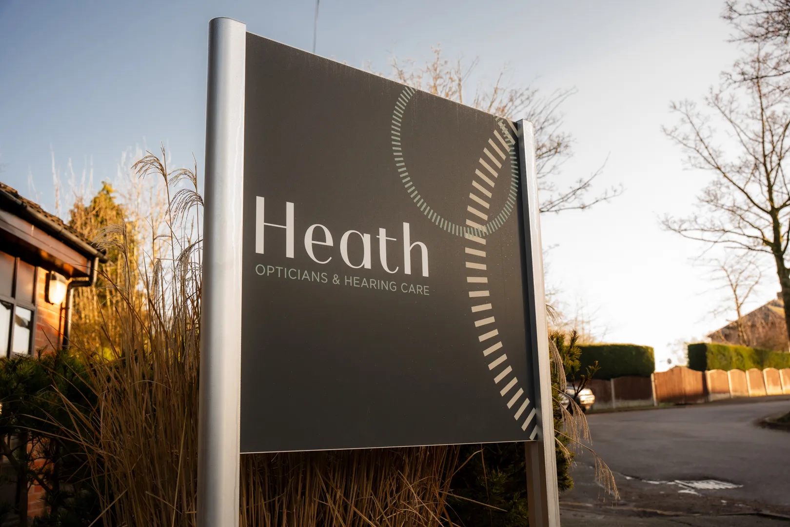 Heath Opticians and Hearing Care business sign displayed outdoors with brick buildings