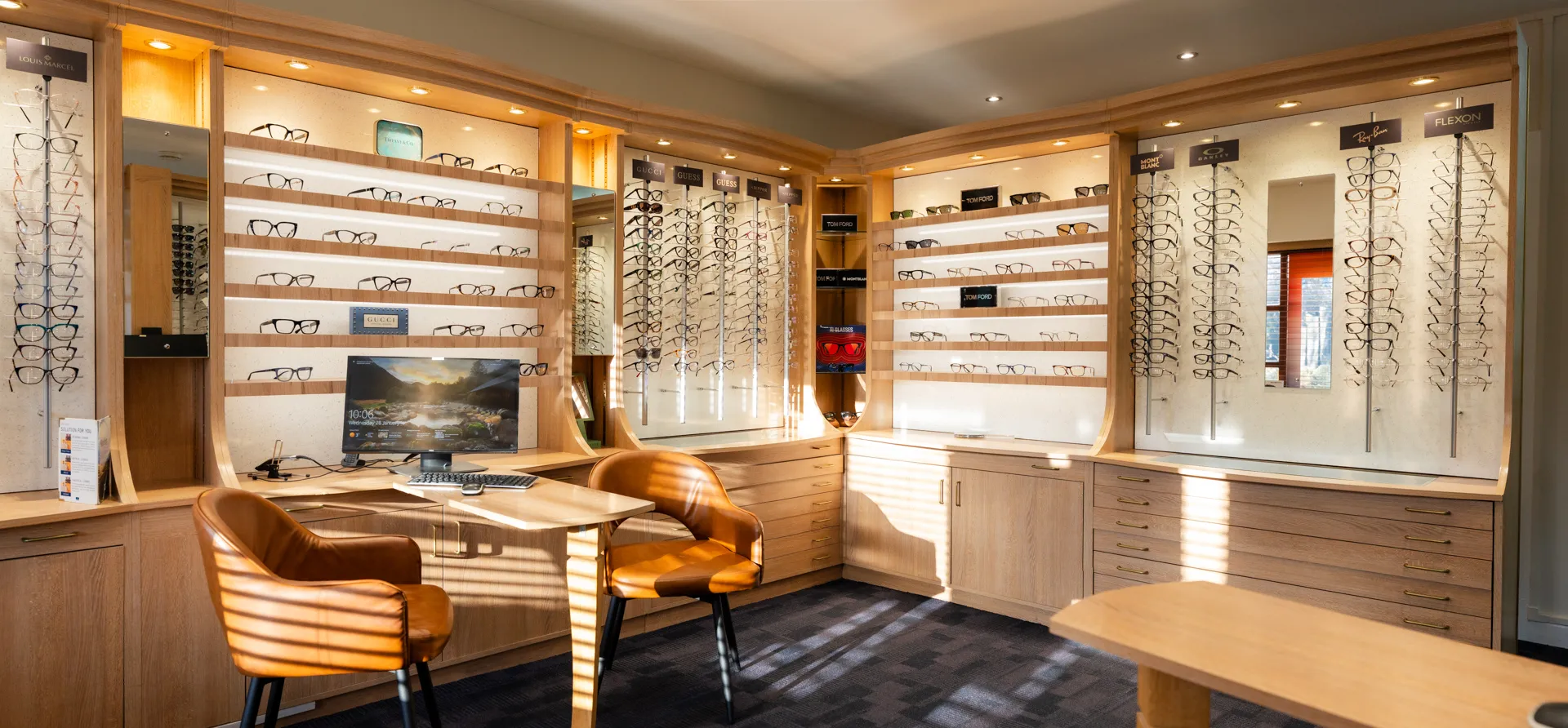 Modern optometry store interior with wooden shelving displaying eyeglasses frames and consultation area.
