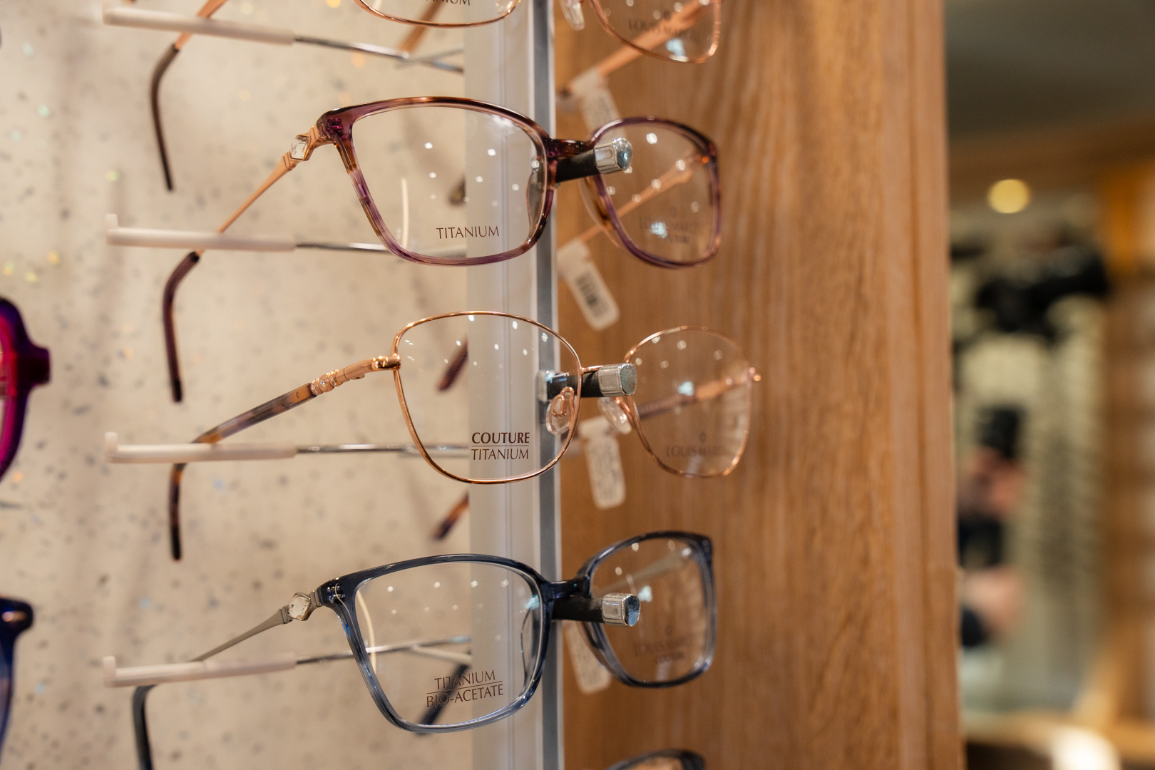 Titanium eyeglasses displayed on white wall rack in optical store showroom