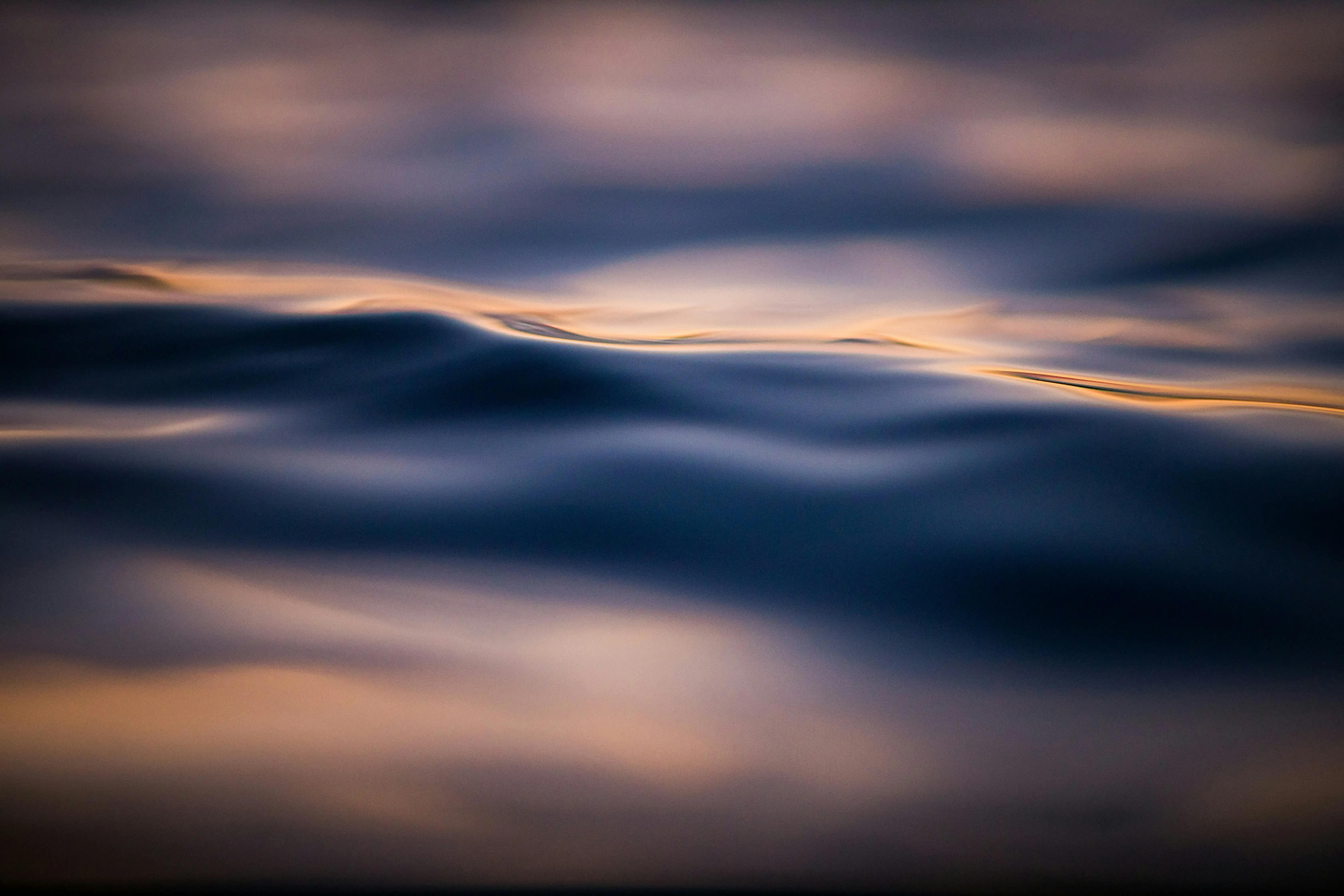Olas suaves en agua oscura reflejando luces doradas y azuladas al atardecer.