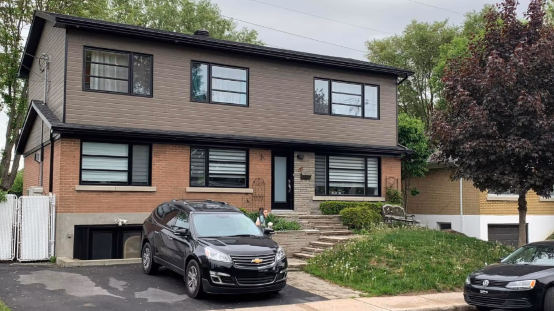 Exterior view of the Crochets residence, showing a two-story home with brick and wood façade, driveway, and parked cars.