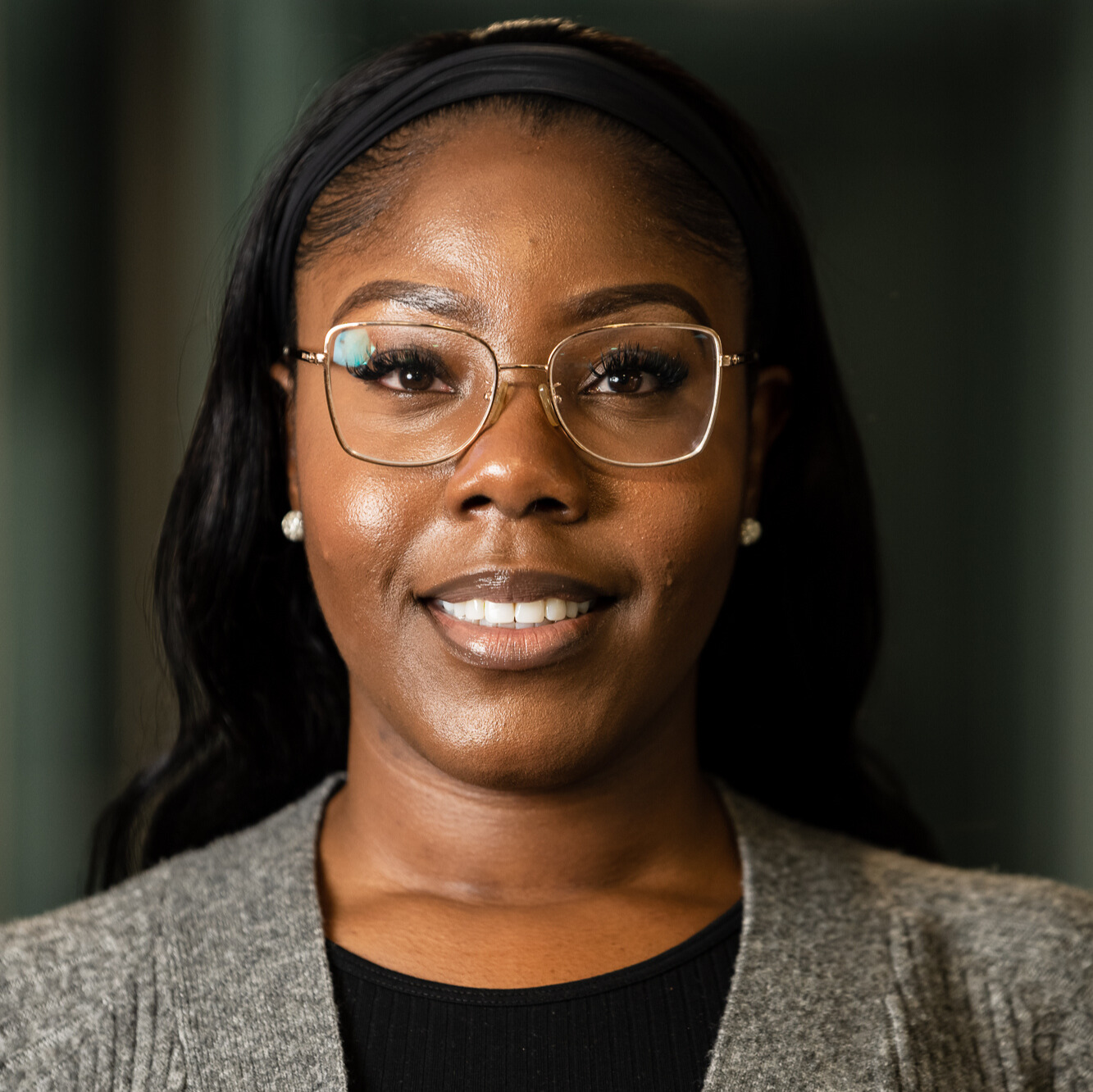 Close-up portrait of a smiling woman with glasses, wearing a gray sweater and black top.