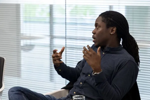 Man with dreadlocks sitting and gesturing with his hands during a conversation in an office setting.