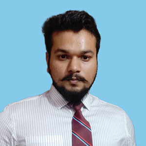 Ujval has dark hair and beard wearing a white striped shirt and red striped tie against a blue background.