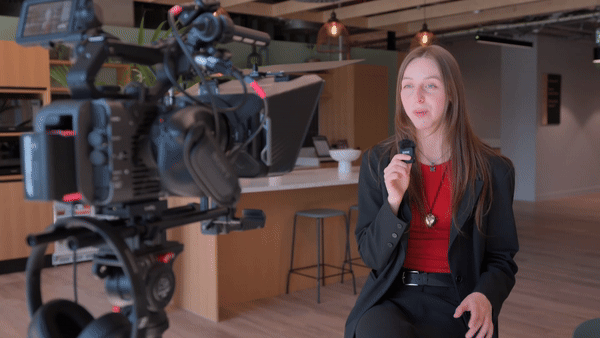 Professional video production of a corporate interview, with a woman speaking on camera using a teleprompter and lapel microphone