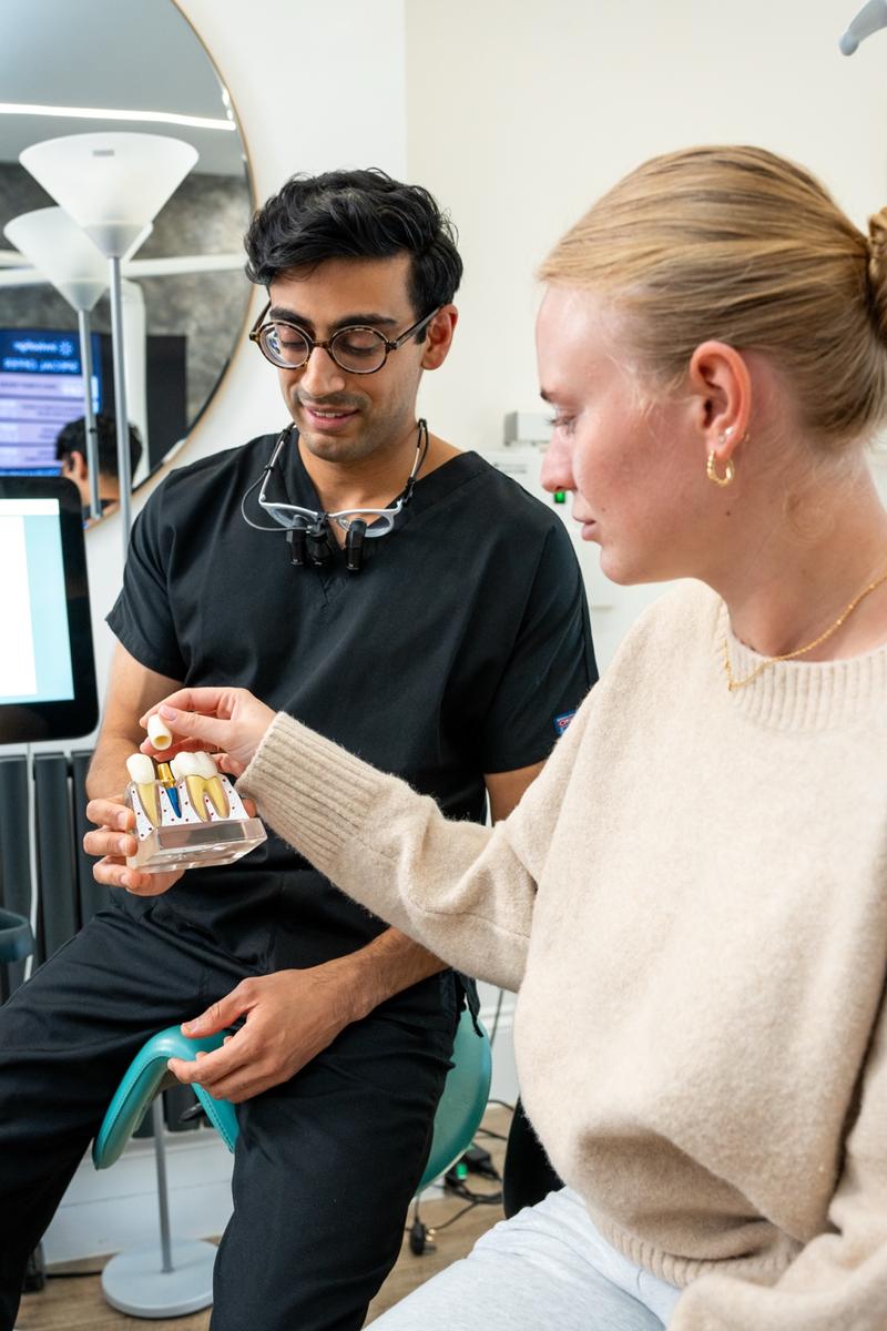 Dentist in black scrubs showing a dental model to a patient who is touching the model.