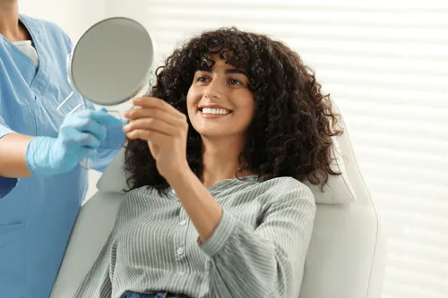 A woman sitting in a dentists chair holding a mirror.