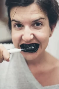 lady with black eyes and short black hair brushing her teeth with charcoal toothpaste solution using an electric tooth brush
