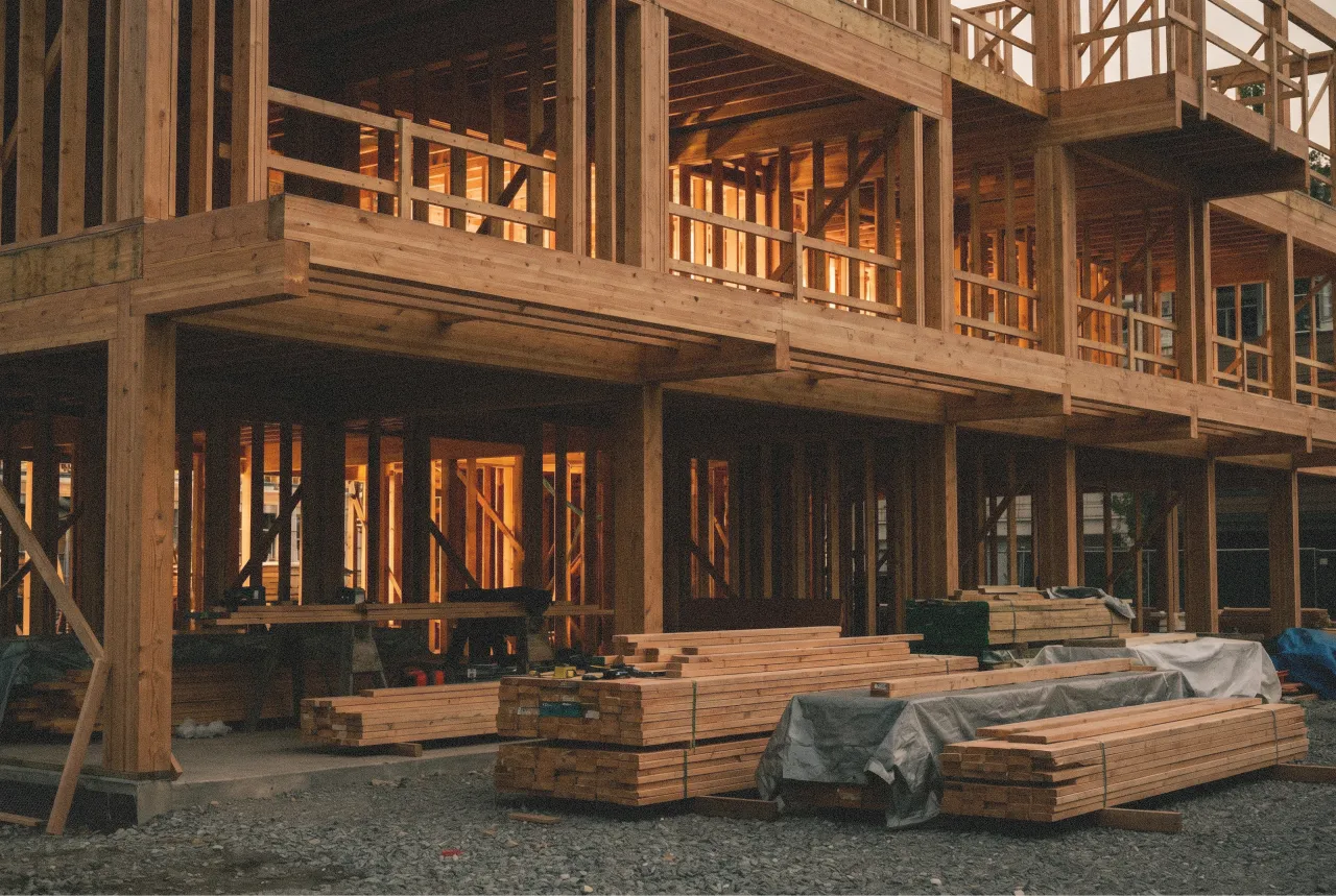 Wooden framework of a multi-story building under construction with stacked lumber outside. Edda Construction.