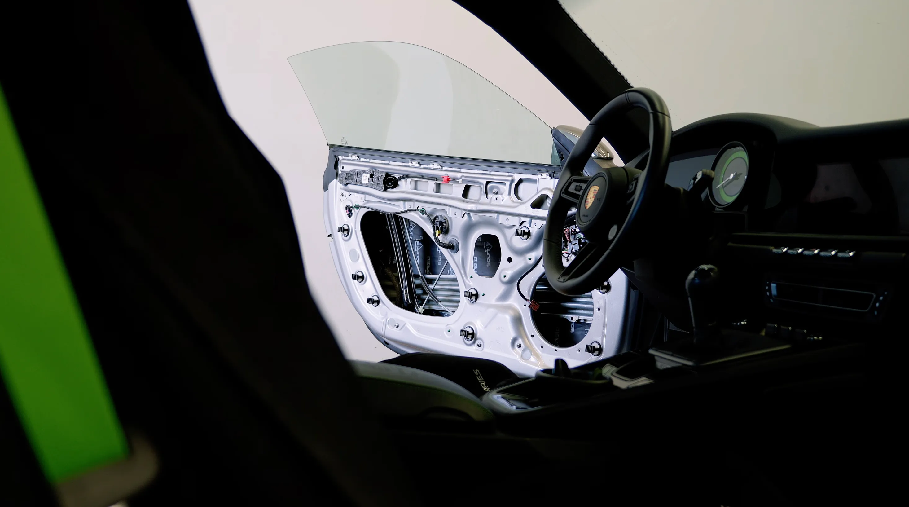 Interior of a car with the driver's side door panel removed showing the metal door frame and wiring being upgraded with sound deadening.
