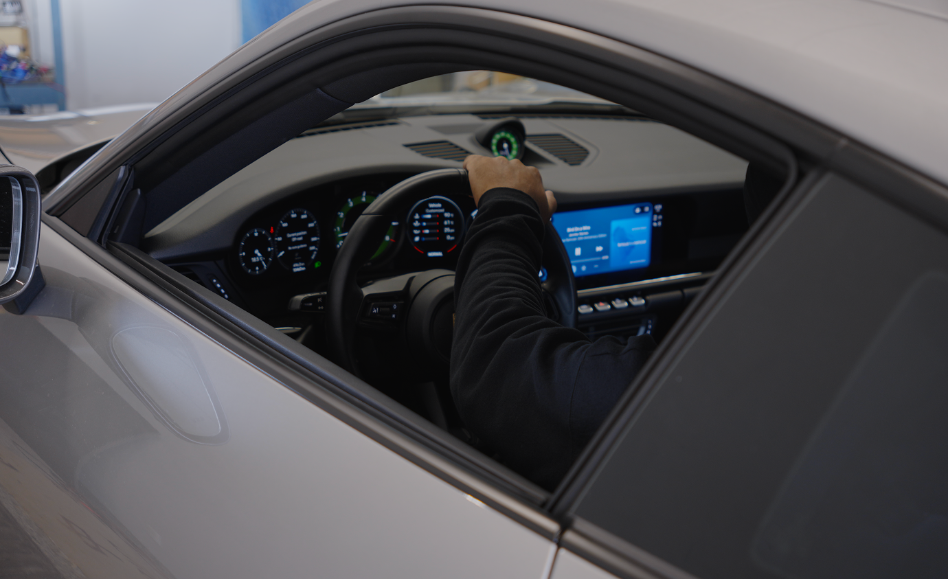 Person's hand on steering wheel of car interior with digital dashboard and infotainment screen.