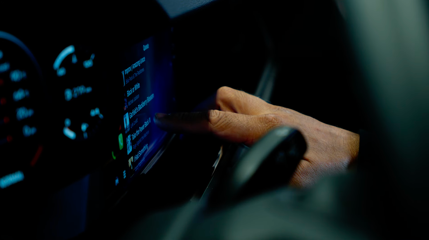Hand touching a car touchscreen displaying music playlist and phone call icons.