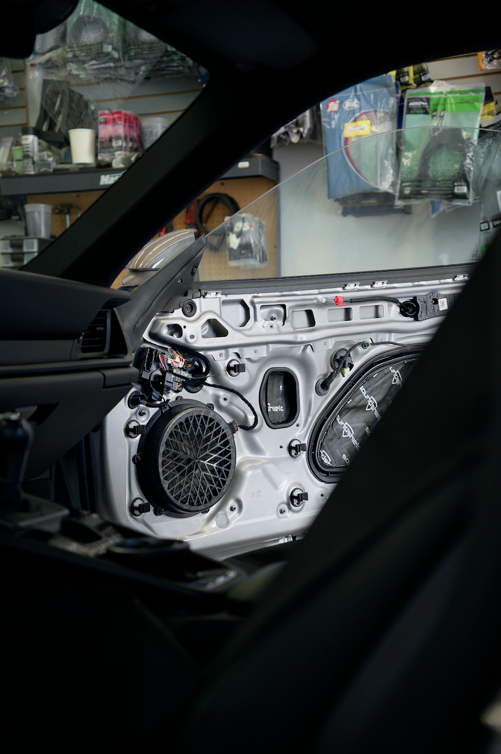 Interior view of a car door with the panel removed showing speaker, wires, and sound deadening.