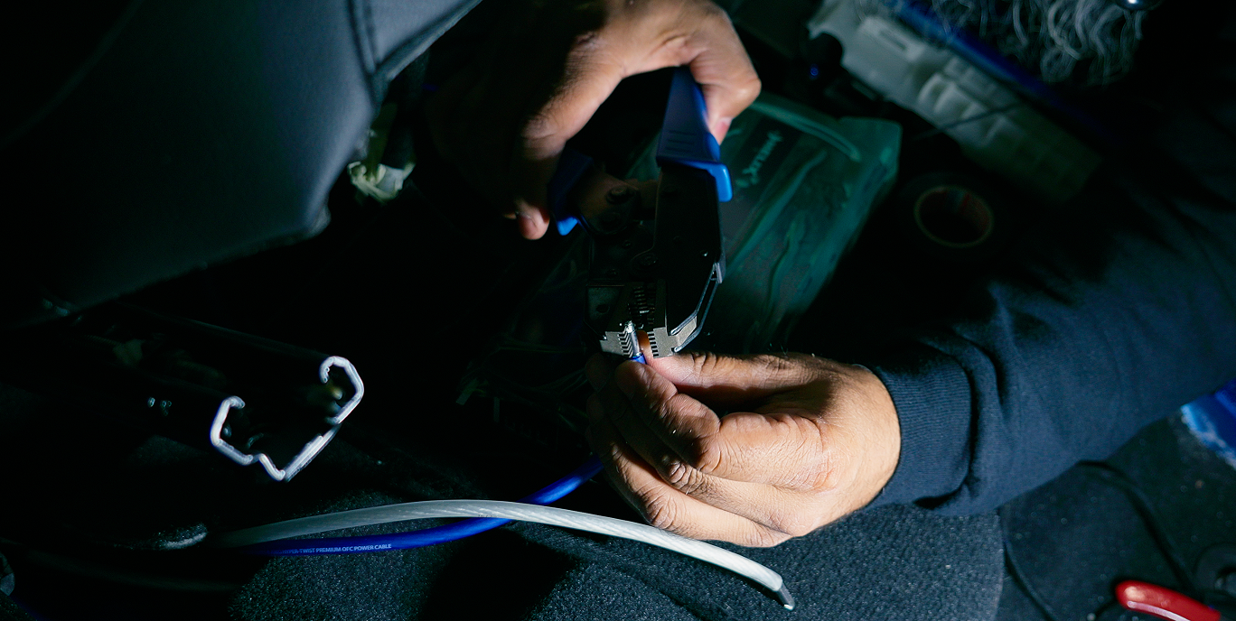 Hands using wire crimping tool on a blue cable with other cables nearby in a dark setting.