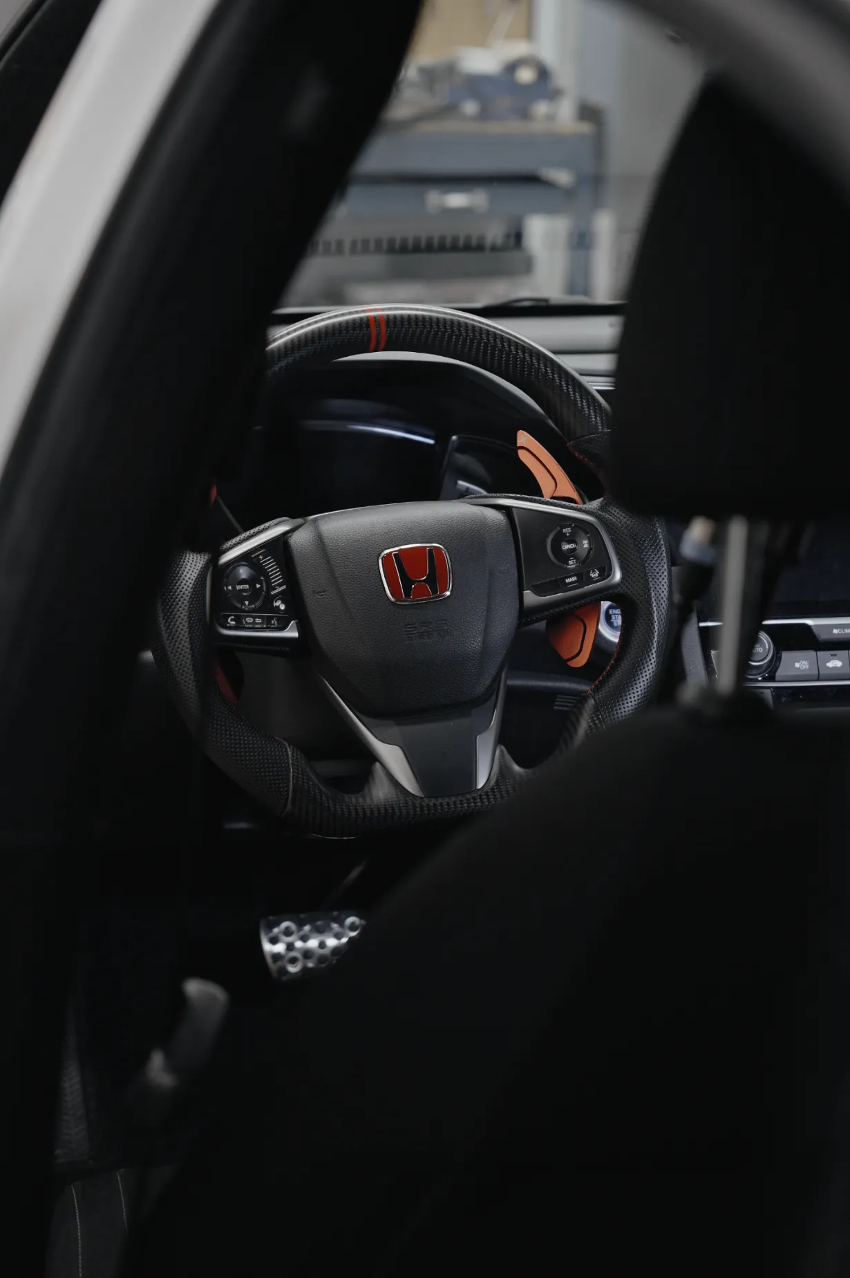 Close-up of a Honda car steering wheel with red accents and dashboard controls behind the seat.