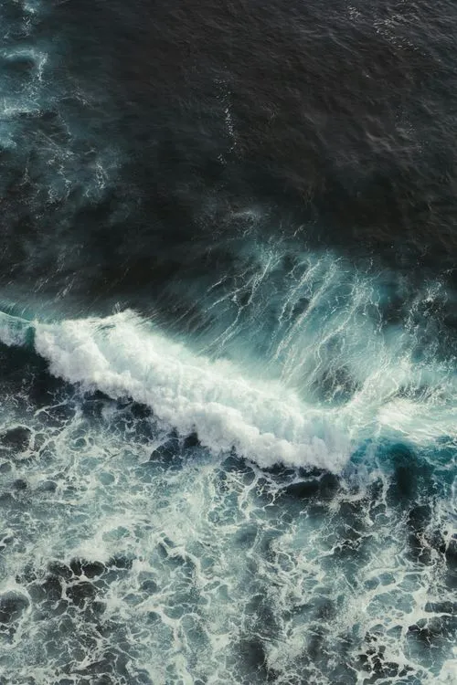 Aerial view of ocean waves crashing and creating white foam on dark blue water.