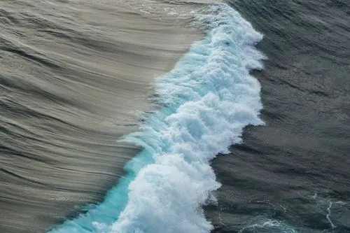 Aerial view of a crashing ocean wave with white foam contrasting against dark water.