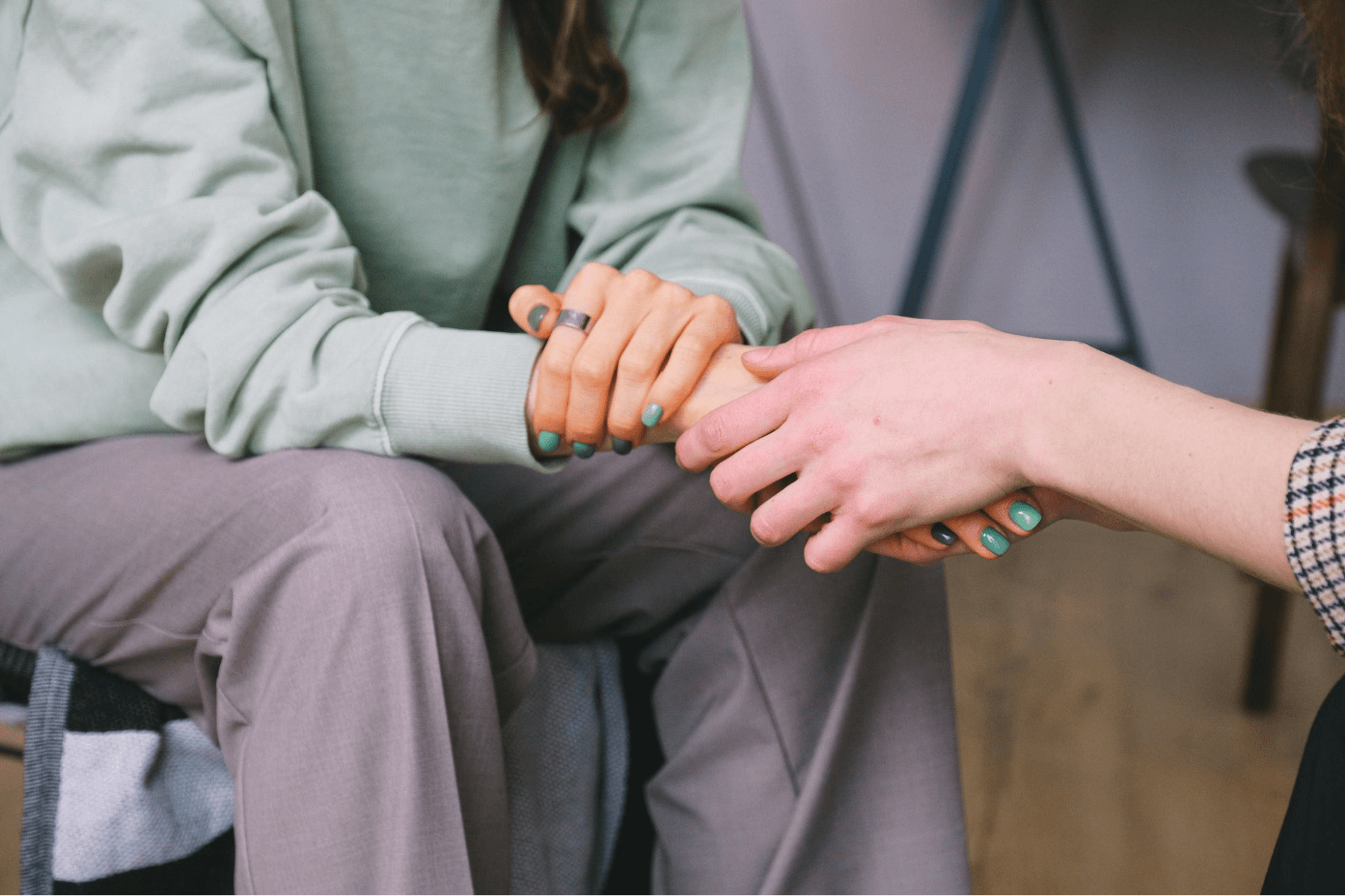 One person is providing support for another by holding their hand. The person on the left is wearing a green sweater and purple pants.
