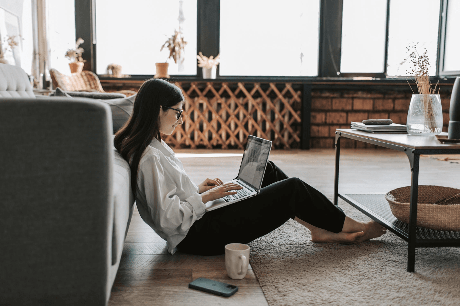 A person is working on their computer. They are sitting on the floor. They are wearing a white top and black pants.