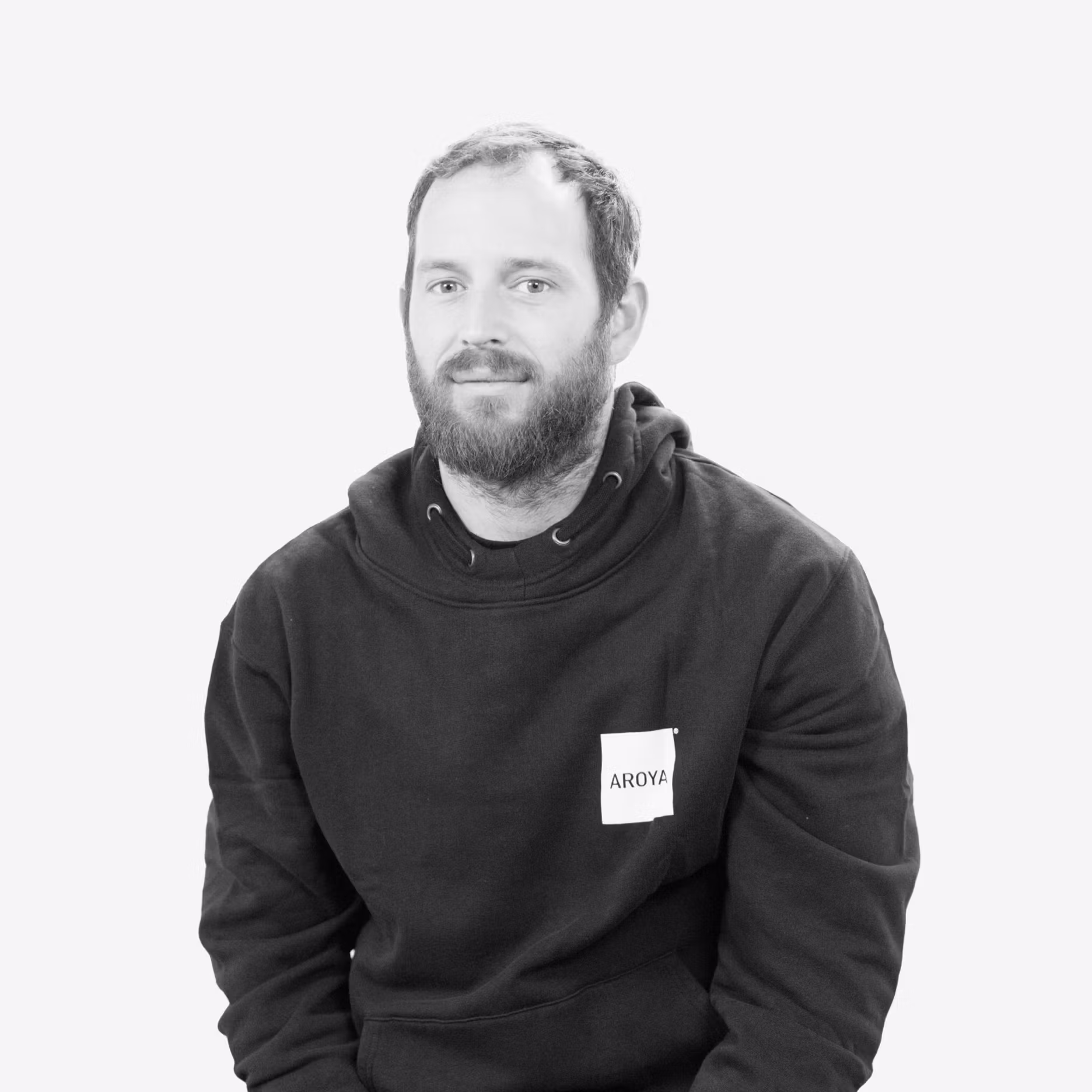 Jason Van Leuven in an AROYA hoodie, photographed in black and white, seated and facing slightly forward with a neutral expression