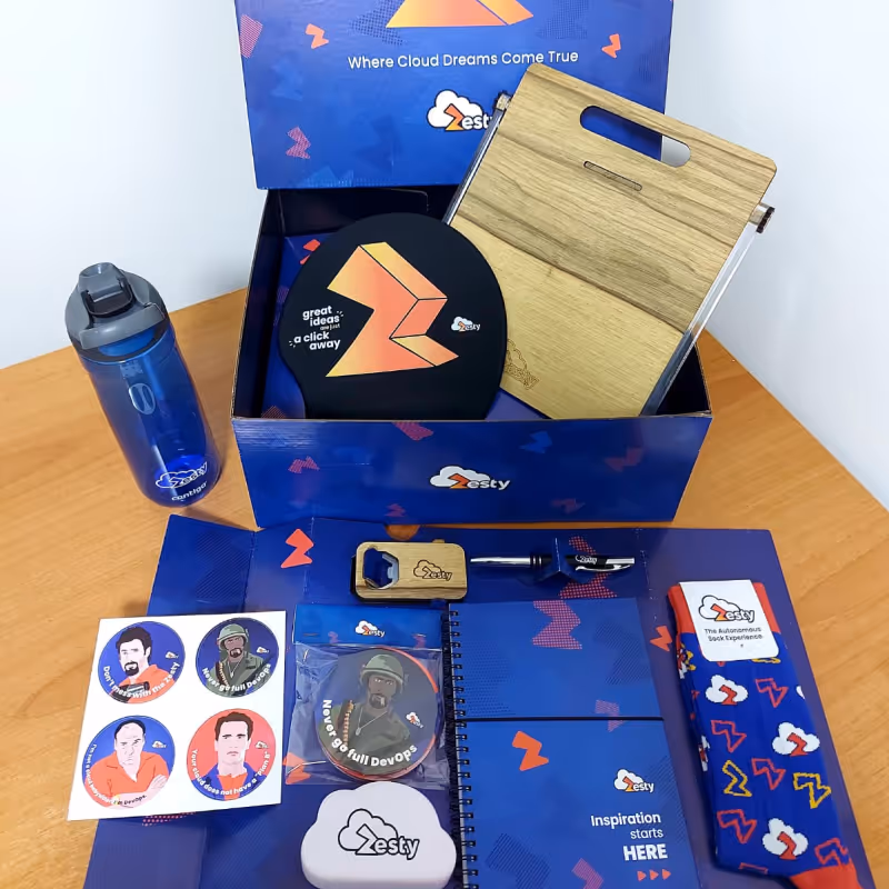Zesty swag box on table containing branded gifts like bottle, socks, notebook, and stickers.