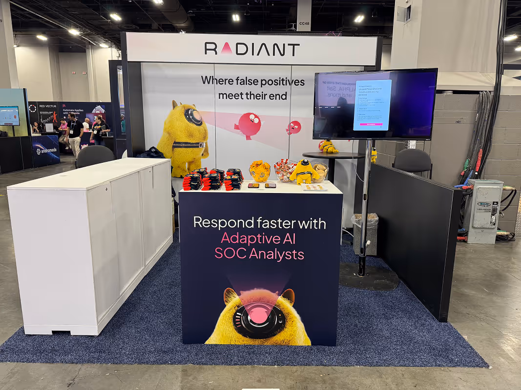 Radiant Security exhibition booth with mascot character, merchandise, and display screen at a tech conference.