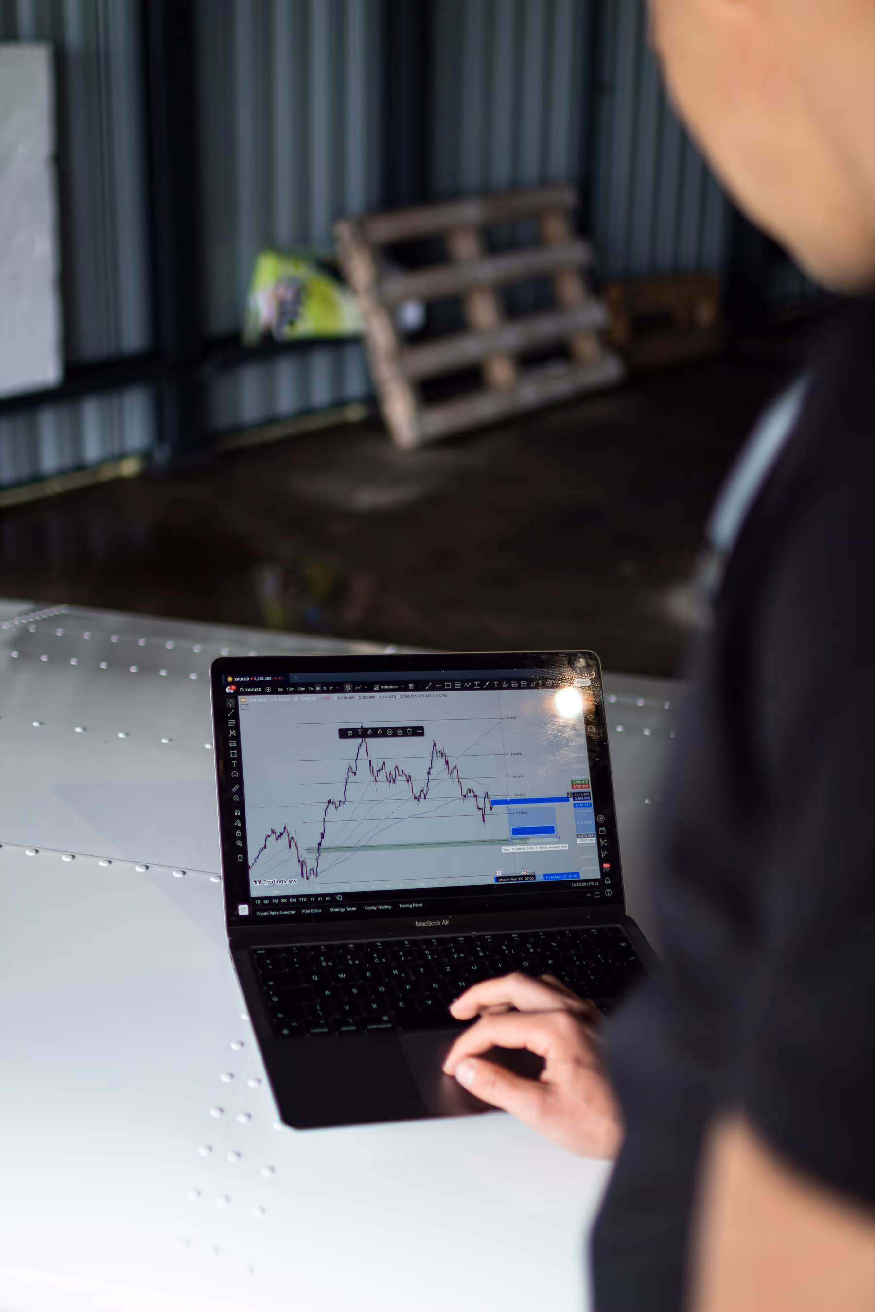 A person analyzes a financial chart on a laptop resting on the wing of an airplane.
