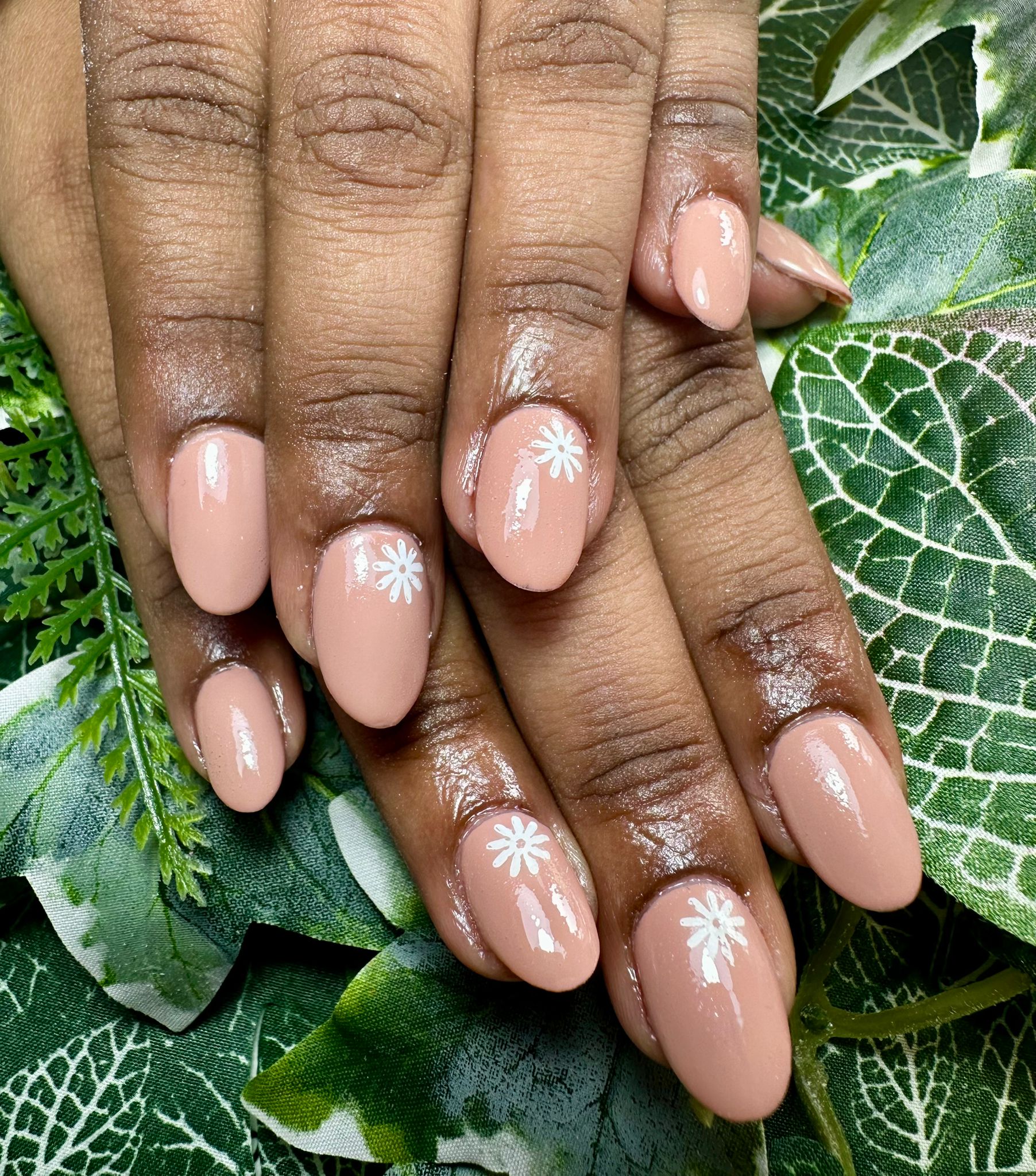 Nude coloured nails with a white flower at the top of each nail.