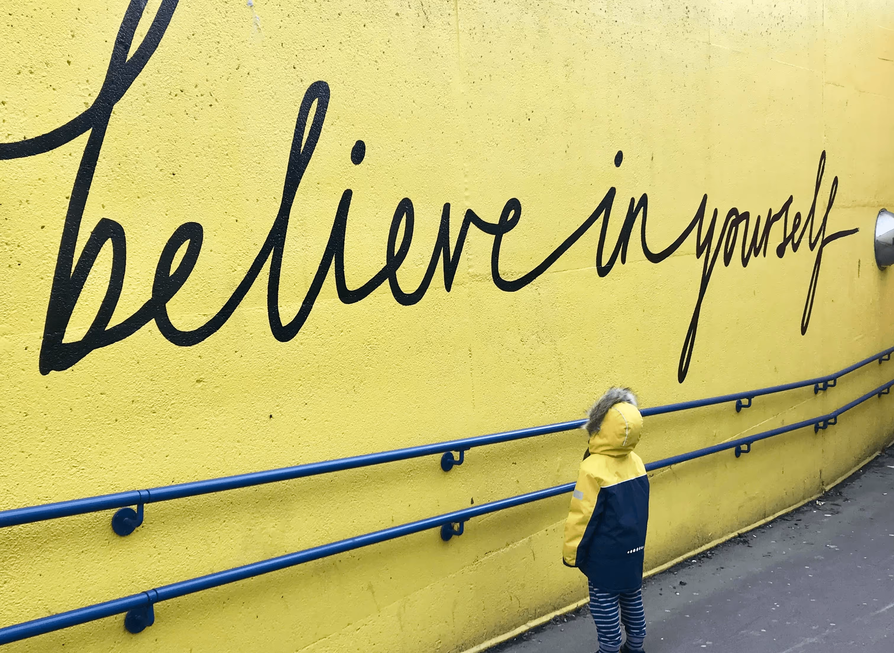 Ein Kind vor einer Mauer, mit dem Schriftzug believe in yourself.