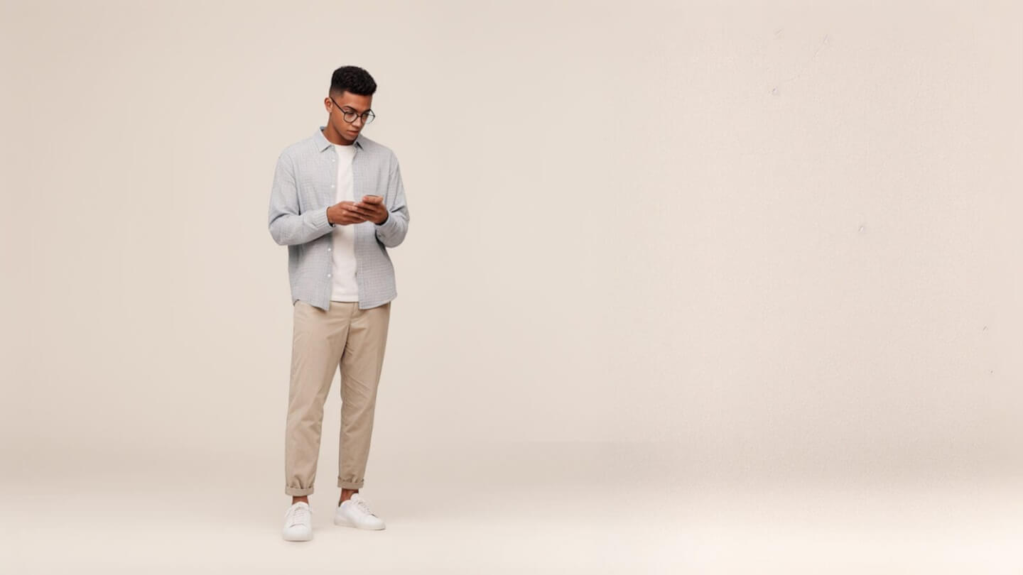 Man in a light shirt and beige trousers looking at his phone in an empty studio.