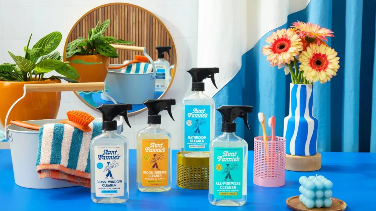 Lineup of plant-based household cleaner spray bottles on a blue counter with flowers and cleaning supplies