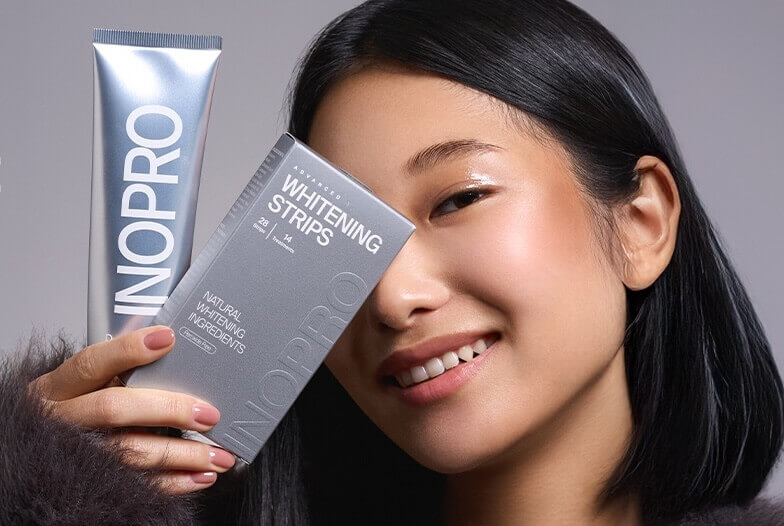 Smiling woman holding teeth whitening strips and a silver toothpaste tube beside her face