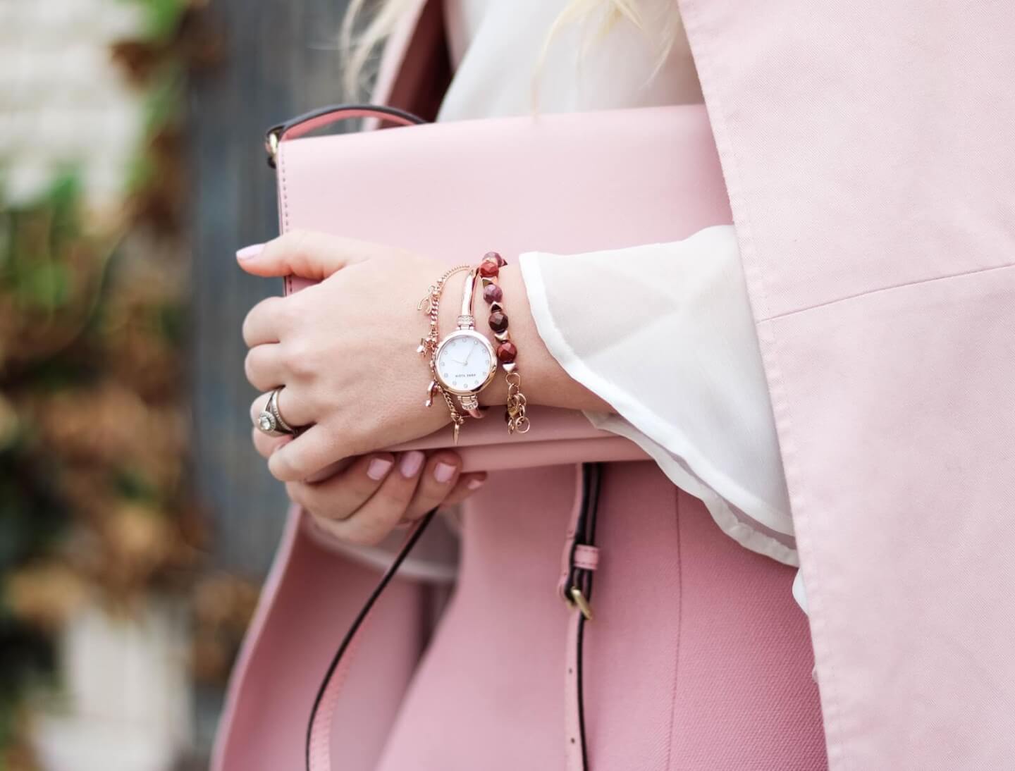 Woman holding a pink handbag, wearing a rose gold watch and beaded bracelets