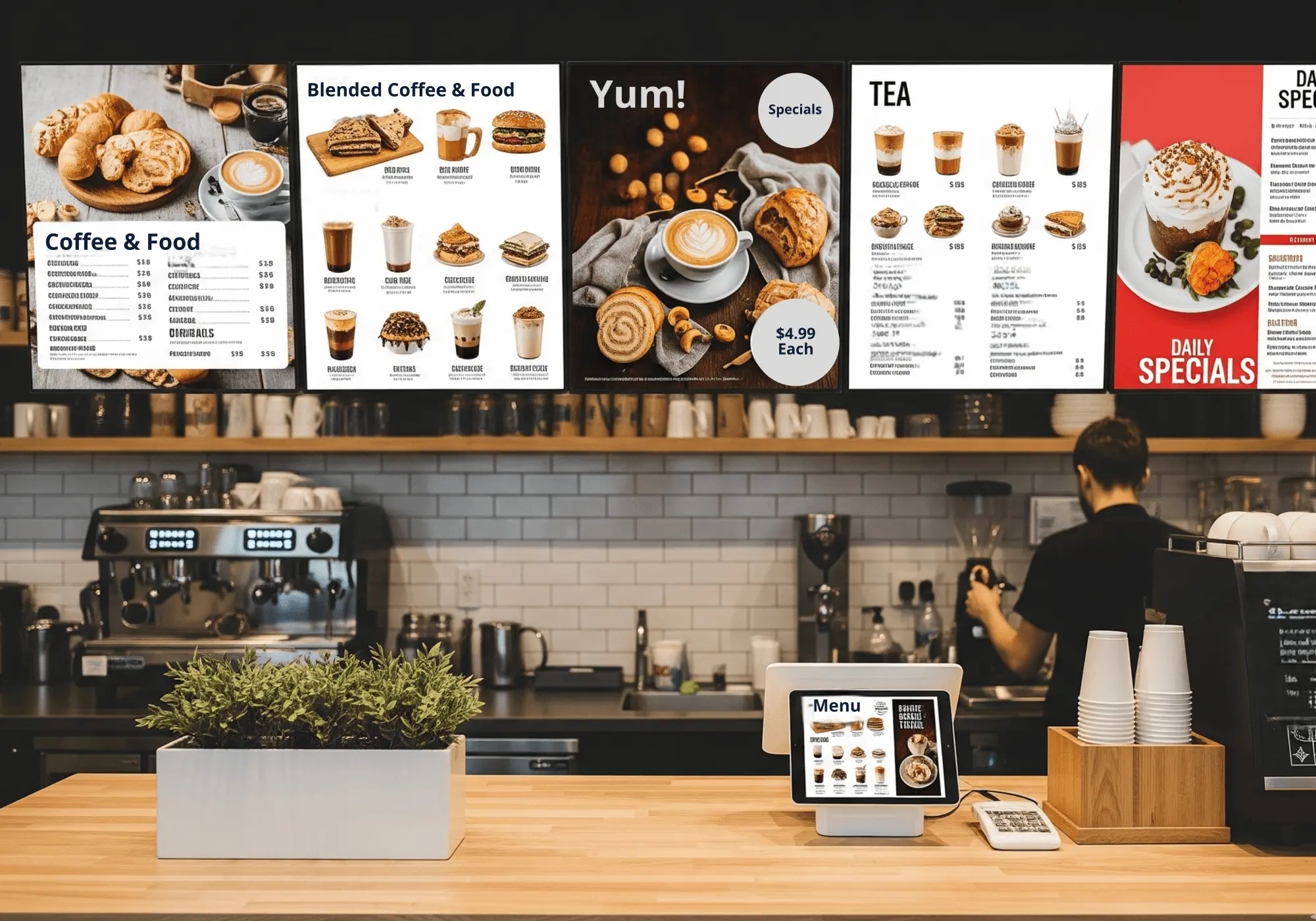 Coffee shop counter with digital menu boards showing coffee, food, tea, and daily specials above a barista preparing drinks.