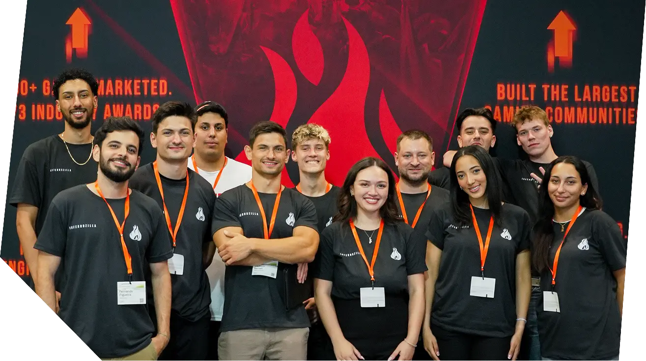 Group of smiling diverse people wearing black shirts and orange badges posing in front of a flame logo backdrop.