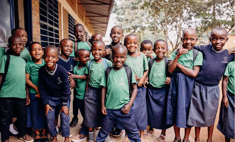 Group of smiling school children in uniforms standing outside school building, posing for photo.