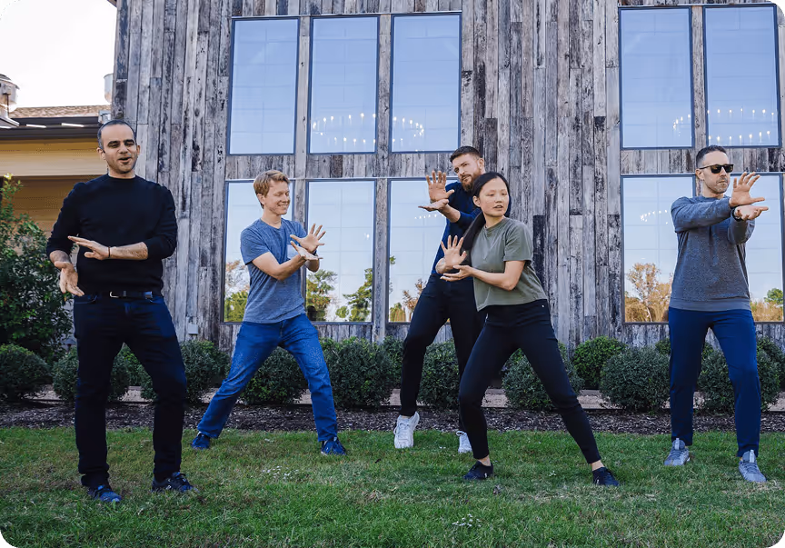 A group of adults standing in front of a large barn and posing for a photo.