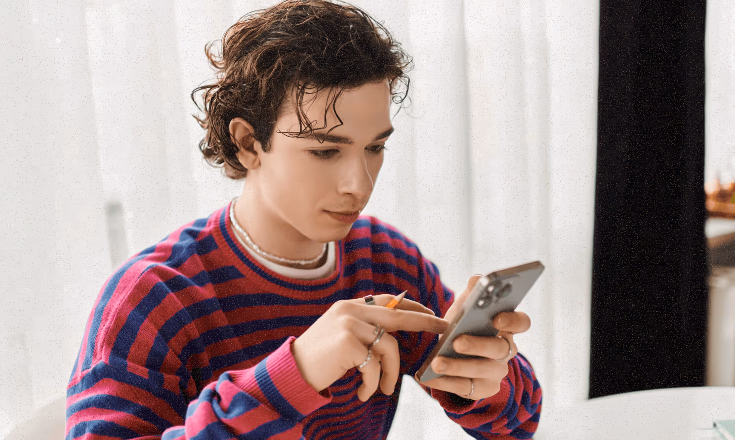 A person holding a pencil and doing work on their smartphone.