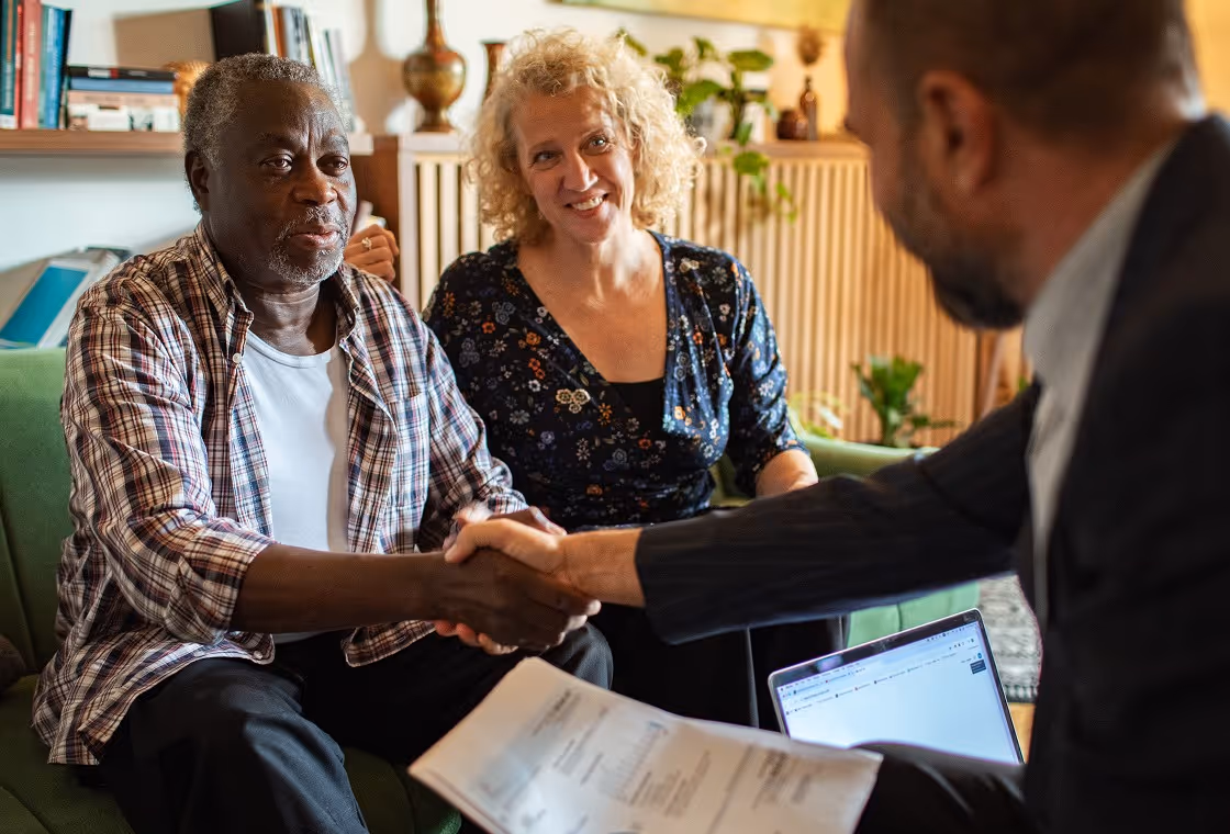 A lawyer leaning across and shaking the hand of a man who is sitting next to his wife.