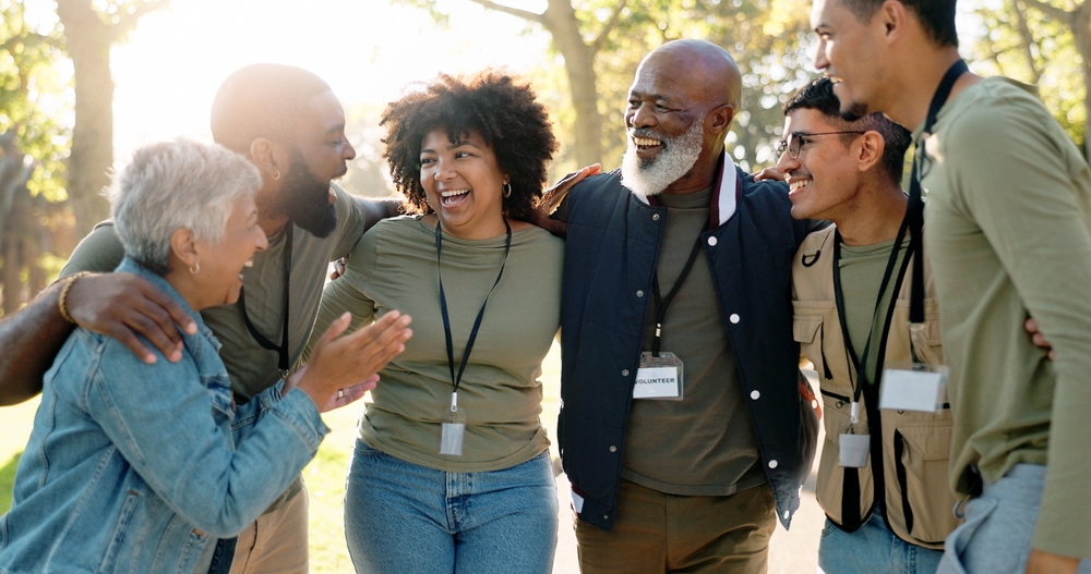 Young man with glasses and wavy hair wearing a black sweater sitting next to a beige wall with dried plants.